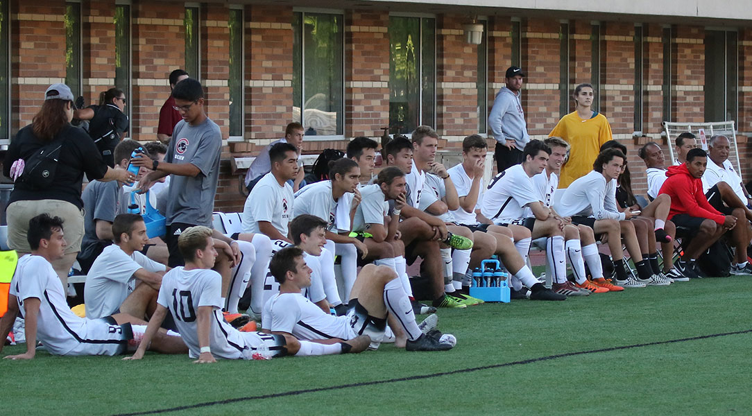 The men's soccer bench looks on.