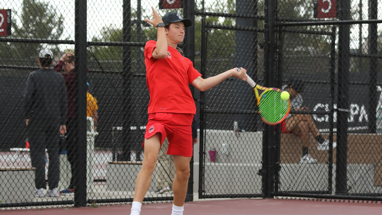 Mac Caldwell swing s his tennis racquet to hit the ball.