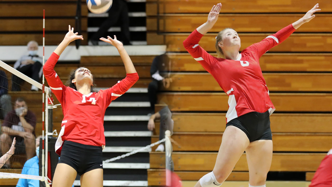 Sophie Srivastava sets and Jessi Lumsden jumps to hit hit a volleyball.
