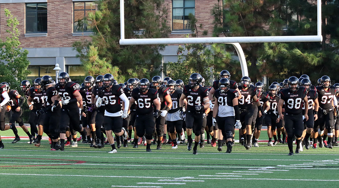 The Chapman football team runs on the field before the game.