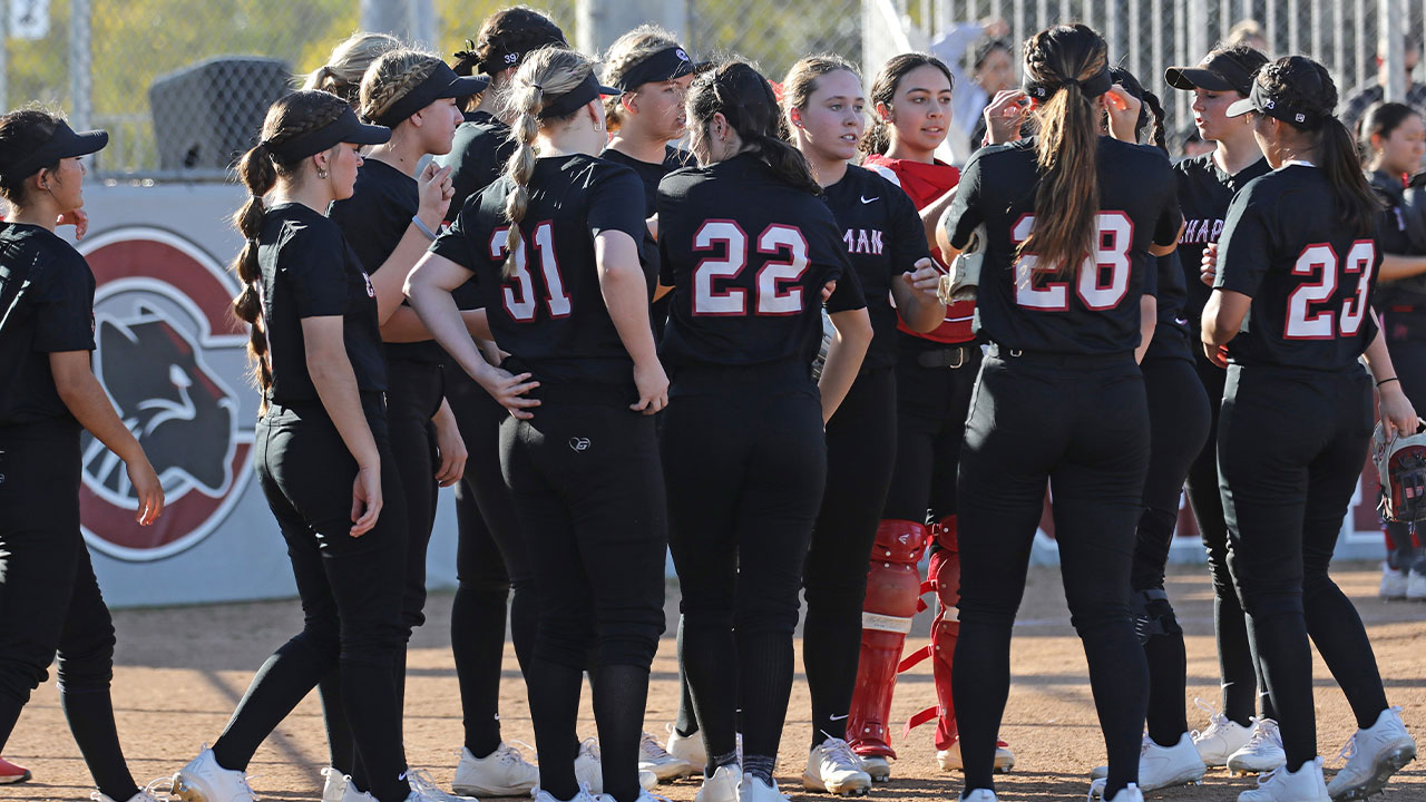 The softball team huddles in front of the dugout.