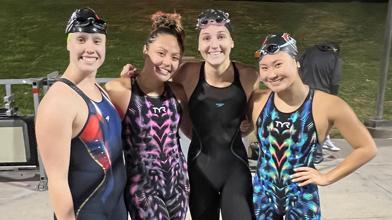 Four swimmers smiling on the pool deck.