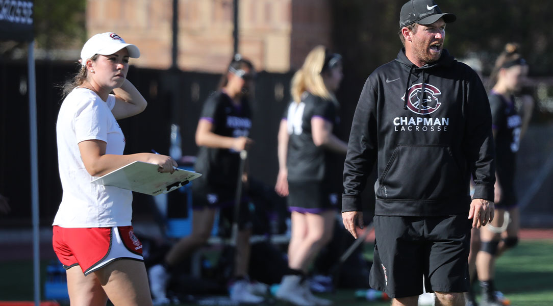 Lacrosse coaches Dan Kirkpatrick and Courtney Novak watch from the sidelines.