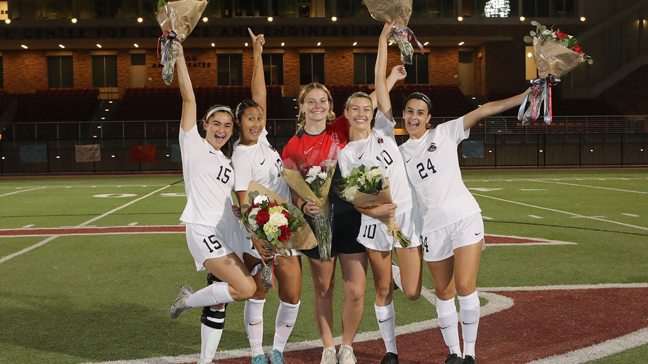 Five women's soccer seniors holding up flowers in celebration.