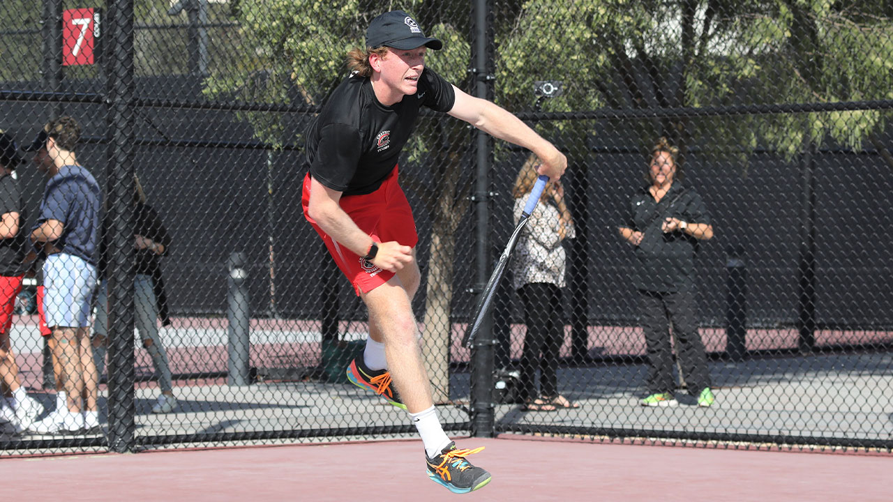 Caleb Wilkins swings hard in his tennis serve.